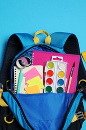 Photo of Backpack with school stationery on light blue background, top view