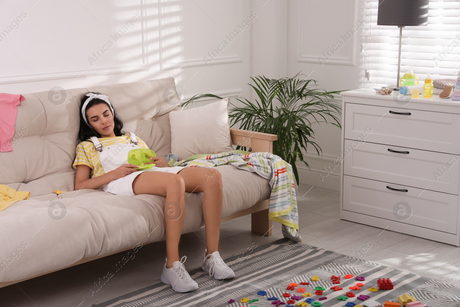 Photo of Tired young mother sleeping on sofa in messy living room