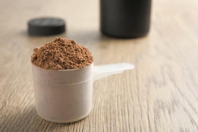Photo of Scoop of chocolate protein powder on wooden table