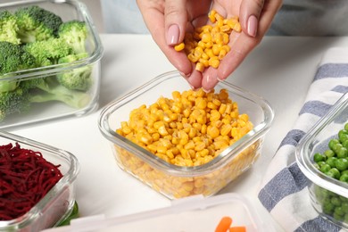 Photo of Woman putting corn into glass container at white table, closeup. Food storage
