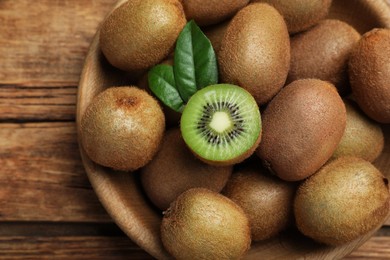 Photo of Bowl with cut and whole fresh kiwis on wooden table, top view
