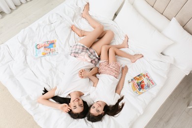Photo of Young mother and her daughter lying on bed at home, top view