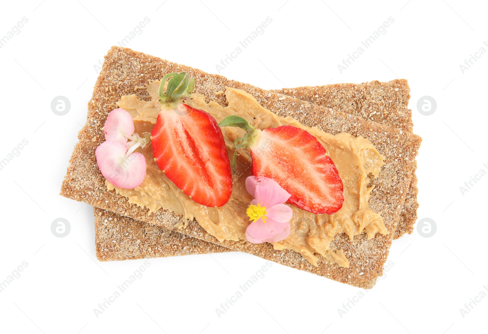 Photo of Fresh rye crispbreads with peanut butter, strawberry and flowers on white background, top view