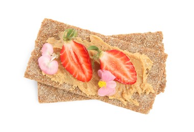 Photo of Fresh rye crispbreads with peanut butter, strawberry and flowers on white background, top view