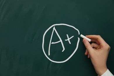 Image of School grade. Teacher encircling letter A and plus symbol with chalk on green chalkboard