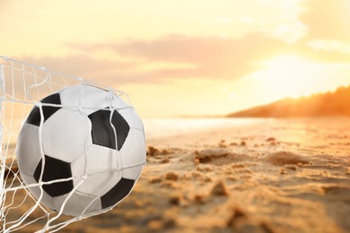 Image of Soccer ball in net on sandy coast near sea. Beach football