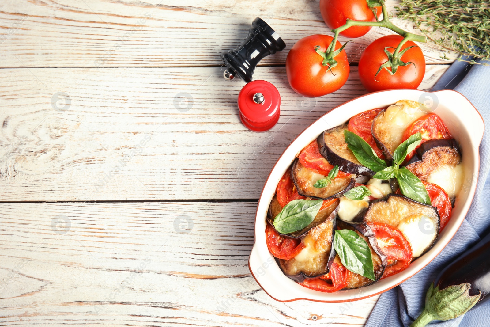 Photo of Flat lay composition with baked eggplant, tomatoes and basil in dishware on wooden table. Space for text