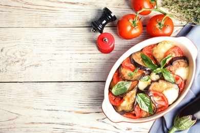 Flat lay composition with baked eggplant, tomatoes and basil in dishware on wooden table. Space for text