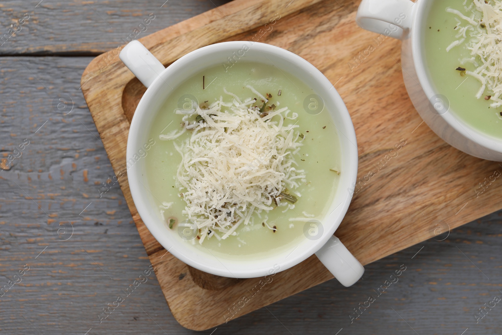 Photo of Delicious cream soup with parmesan cheese in bowls on grey wooden table, flat lay