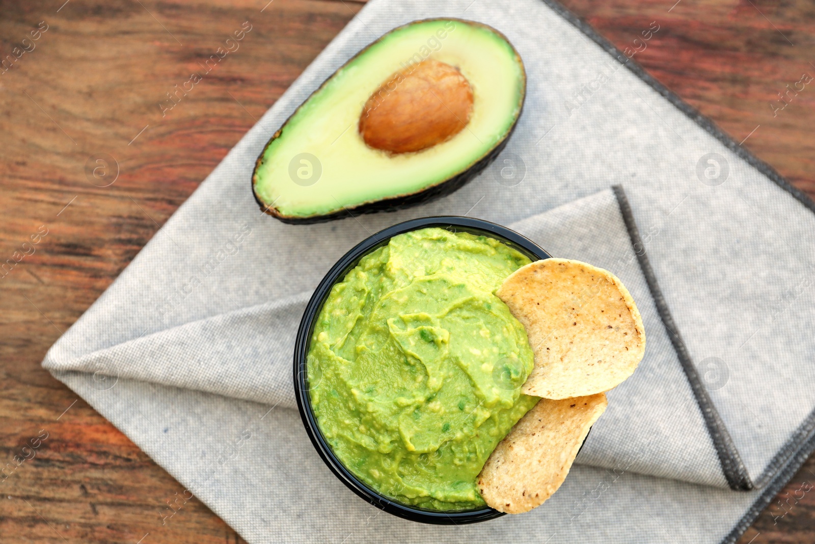 Photo of Delicious guacamole made of avocados with nachos and cut fruit on wooden table, flat lay