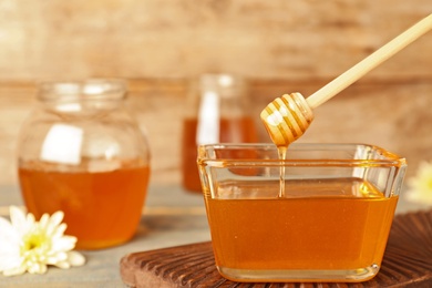 Honey dripping from dipper into glass bowl on wooden table