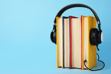 Photo of Books and modern headphones on light blue background. Space for text