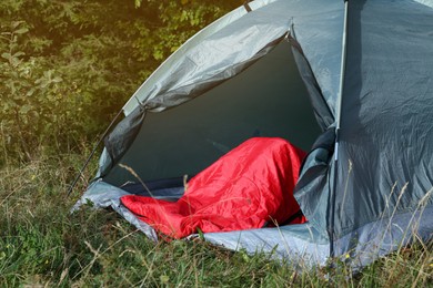 Photo of Red sleeping bag in camping tent on green grass outdoors