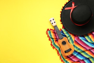 Photo of Mexican sombrero hat, guitar and colorful poncho on yellow background, flat lay. Space for text