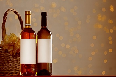 Photo of Bottles of wine and wicker basket with bow against blurred lights. Space for text