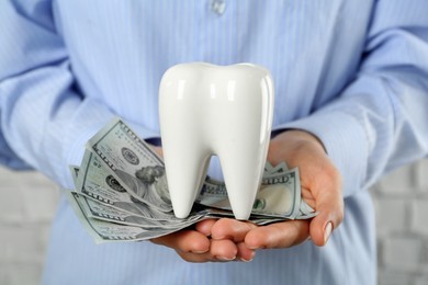 Photo of Woman holding ceramic model of tooth and dollar banknotes on light background, closeup. Expensive treatment
