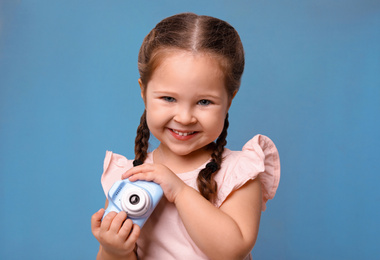 Little photographer with toy camera on light blue background