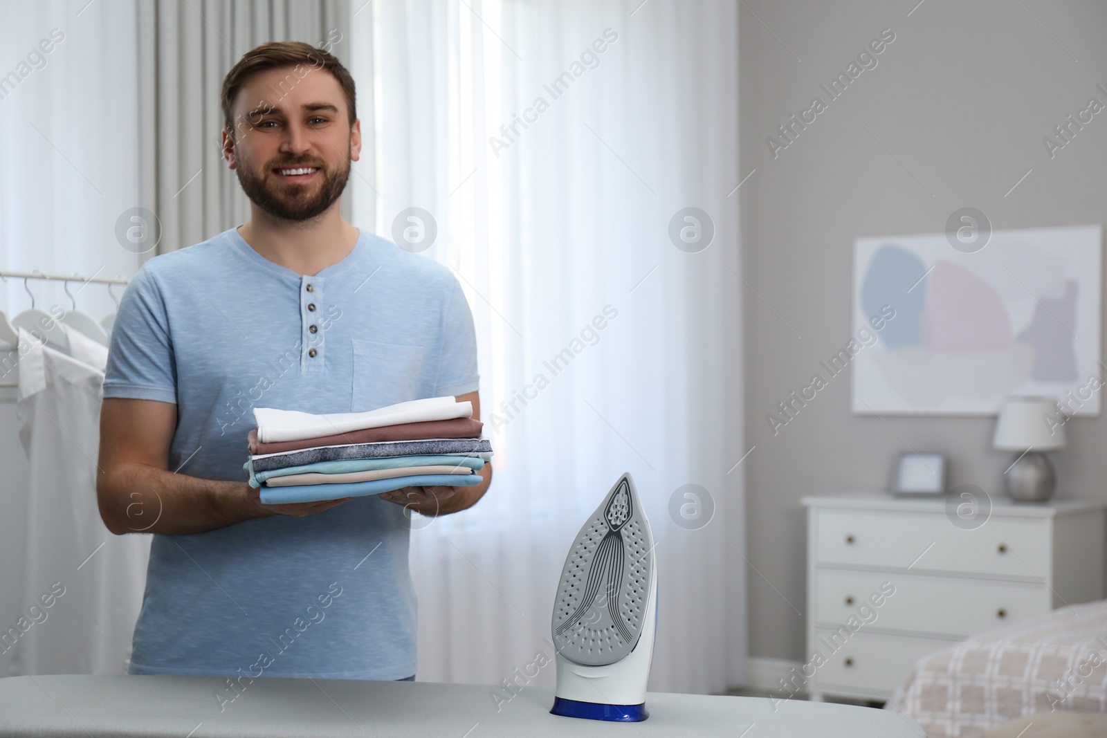 Photo of Man with folded clothes after ironing near board at home. Space for text