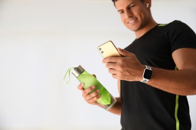 Man with smartphone and fitness tracker in gym, focus on hand