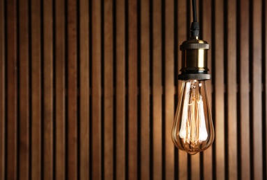 Pendant lamp with light bulb near wooden wall, space for text