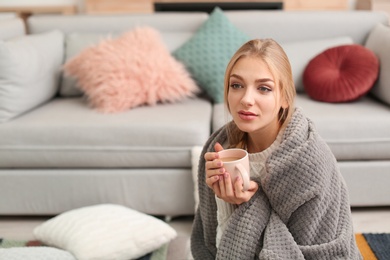 Photo of Beautiful young woman wrapped in plaid sitting with cup of coffee on floor at home. Winter atmosphere