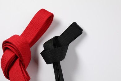 Photo of Red and black karate belts on white background, flat lay. Space for text