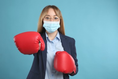 Businesswoman with protective mask and boxing gloves on light blue background. Strong immunity concept