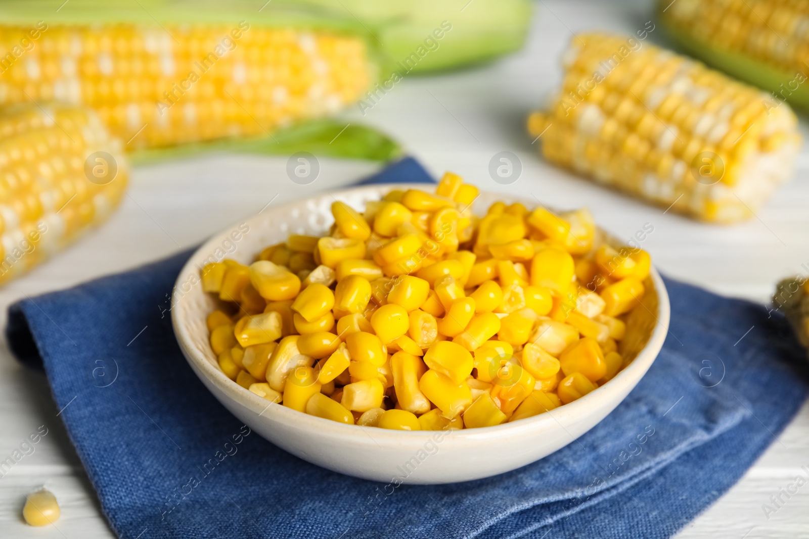 Photo of Tasty sweet corn kernels in bowl and fresh cobs on table