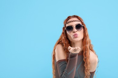 Photo of Stylish young hippie woman in sunglasses blowing kiss on light blue background, space for text