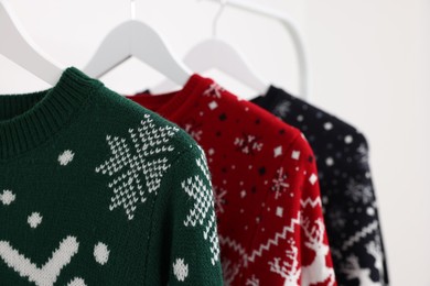 Different Christmas sweaters hanging on rack against white background, closeup