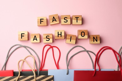 Photo of Empty wooden cubes and different shopping bags on pink background, flat lay