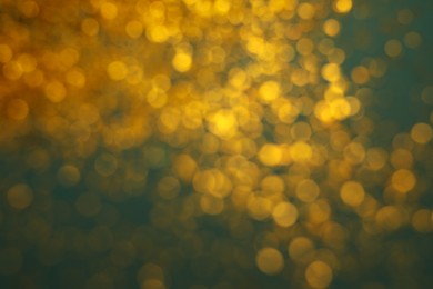 Blurred view of golden glitter on green background. Bokeh effect