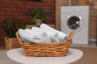 Photo of Wicker basket with folded towels on white table in laundry room