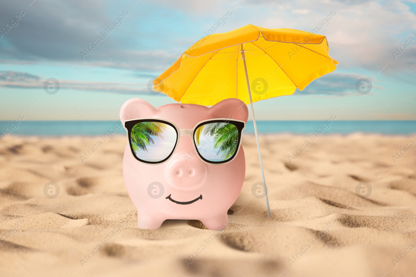 Image of Vacation savings. Piggy bank near umbrella on sandy beach near sea. Reflection of palm leaves in sunglasses