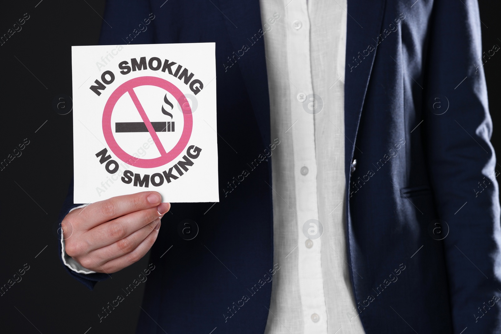 Photo of Woman holding card with no smoking sign on black background, closeup