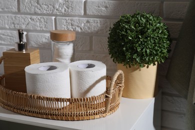 Photo of Toilet paper rolls, floral decor, dispenser and cotton pads on chest of drawers indoors