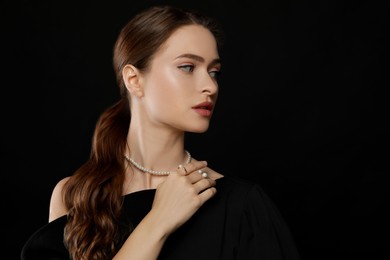 Photo of Young woman wearing elegant pearl jewelry on black background, space for text