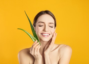 Photo of Happy young woman with aloe leaves on yellow background