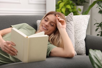 Photo of Woman reading book on sofa in room with houseplants