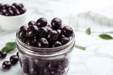 Fresh acai berries in glass jar on white table, closeup