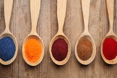 Photo of Many spoons with food coloring on wooden table, flat lay