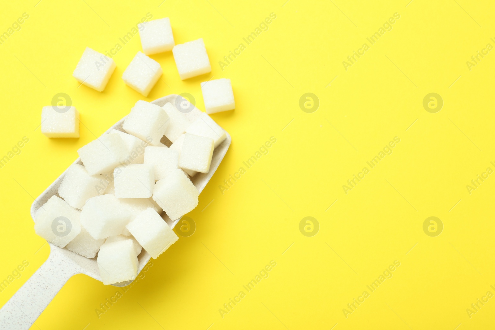 Photo of White sugar cubes and scoop on yellow background, top view. Space for text