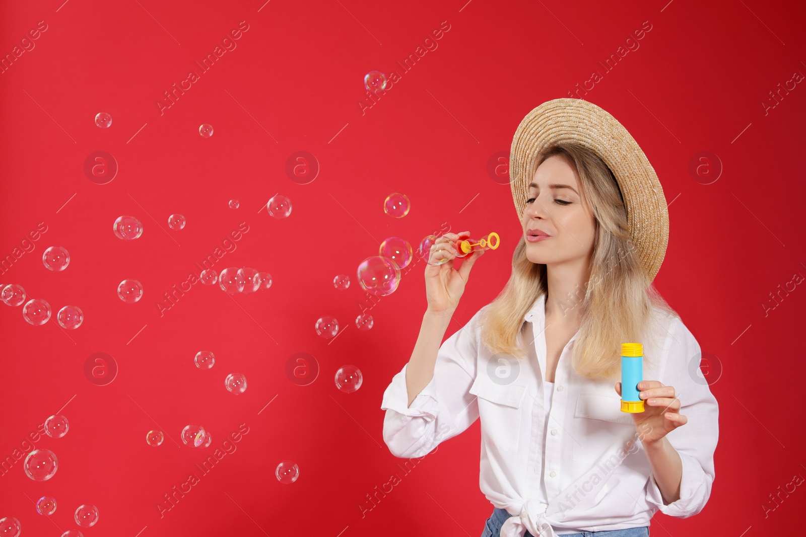 Photo of Young woman blowing soap bubbles on red background, space for text