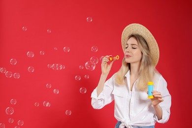 Young woman blowing soap bubbles on red background, space for text