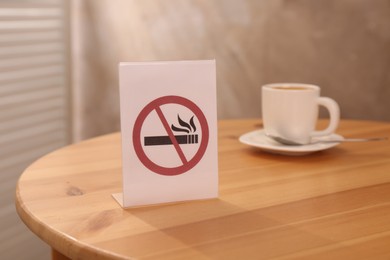 Photo of No Smoking sign and cup of drink on wooden table indoors, selective focus