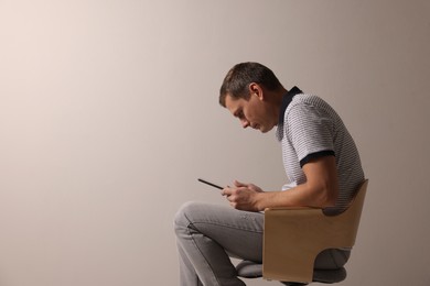 Photo of Man with bad posture using tablet while sitting on chair against grey background. Space for text