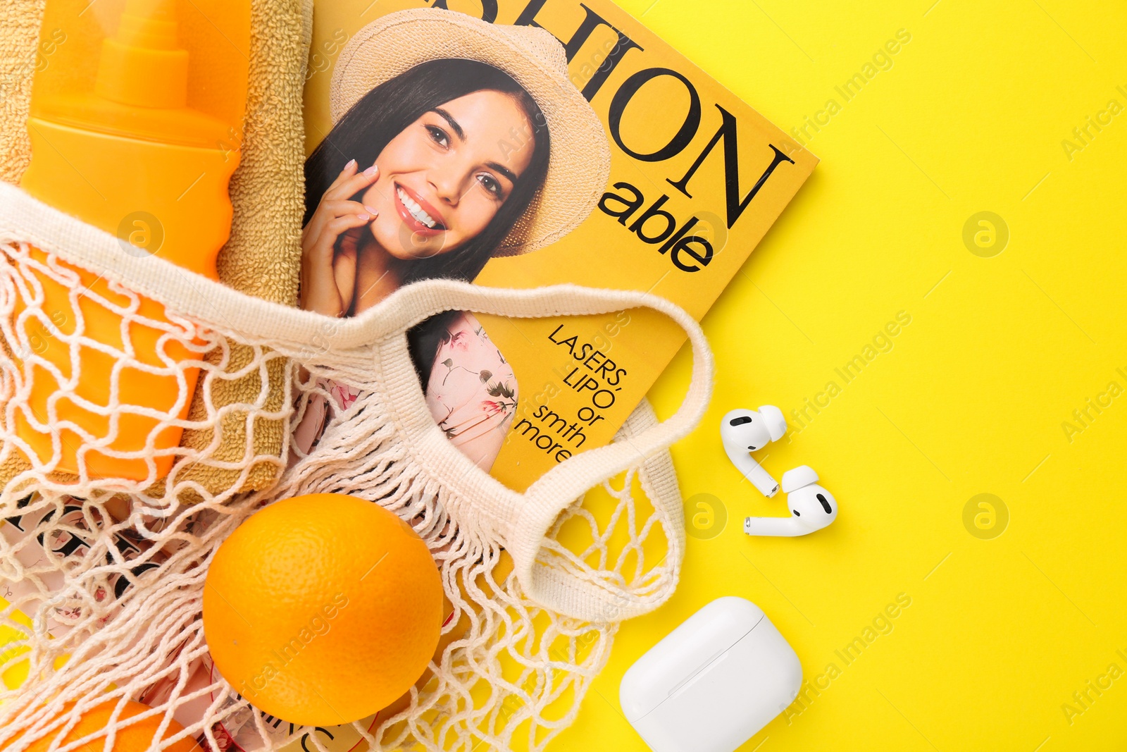 Photo of String bag with fresh oranges, fashion magazine and beach accessories on yellow background, flat lay. Space for text