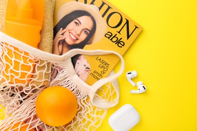 String bag with fresh oranges, fashion magazine and beach accessories on yellow background, flat lay. Space for text