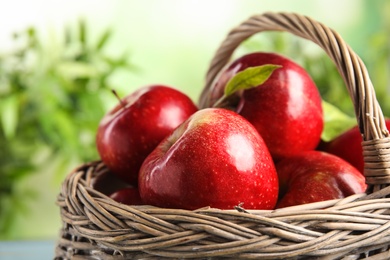 Wicker basket with ripe juicy red apples against blurred background, closeup