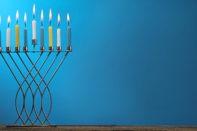 Photo of Hanukkah celebration. Menorah with burning candles on table against light blue background, space for text